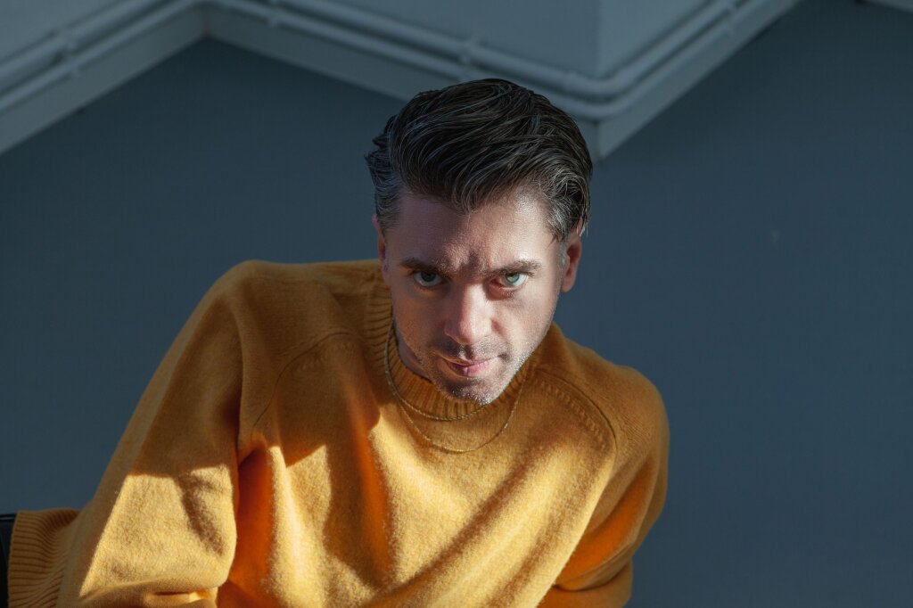 Portrait of the musician Die Wilde Jagd wearing a yellow sweatshirt looking into the camera.