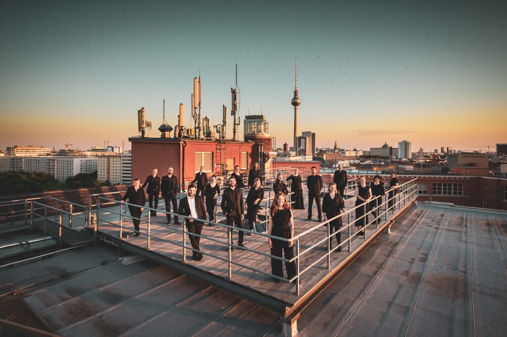 The Neuer Kammerchor Berlin choir standing on a rooftop in Berlin, Alex and a sunset behind them.