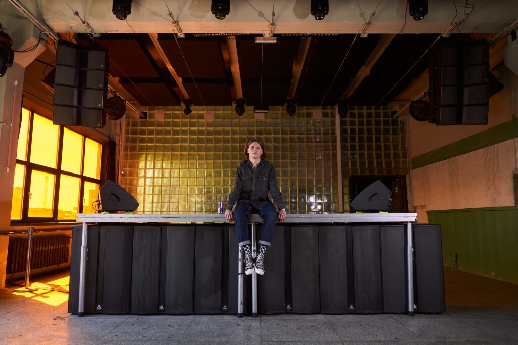 A man sitting on a DJ booth and looking directly into the camera.