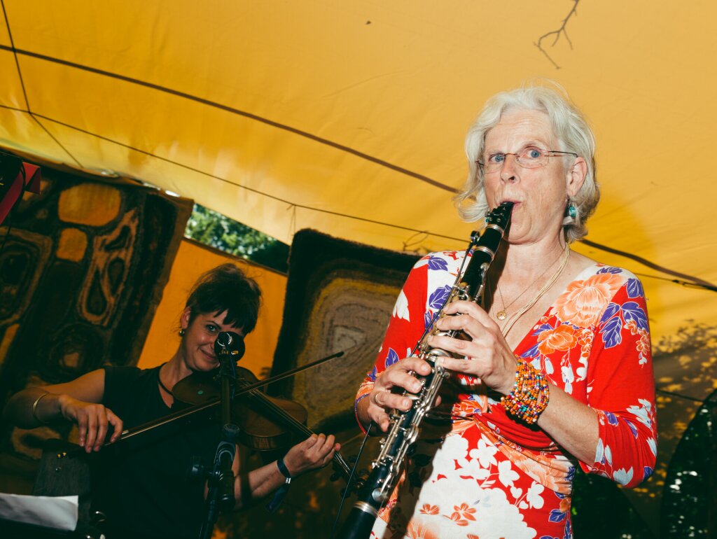 An elderly woman is playing the clarinet, a woman with a violin behind her.